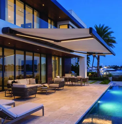 lit retractable awning over a waterfront pool terrace at dusk
